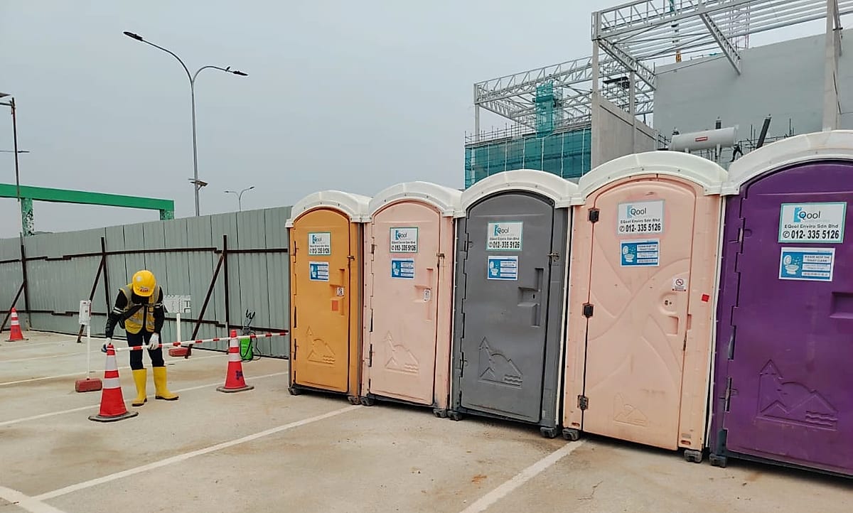 Row of EQool portable toilets with a worker setting up safety barriers and cones