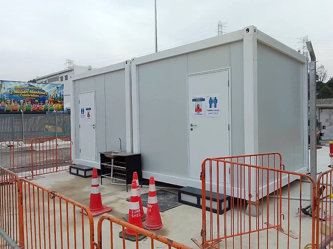 White EQool container toilet cabins with a hand-wash sink, traffic cones and orange barriers