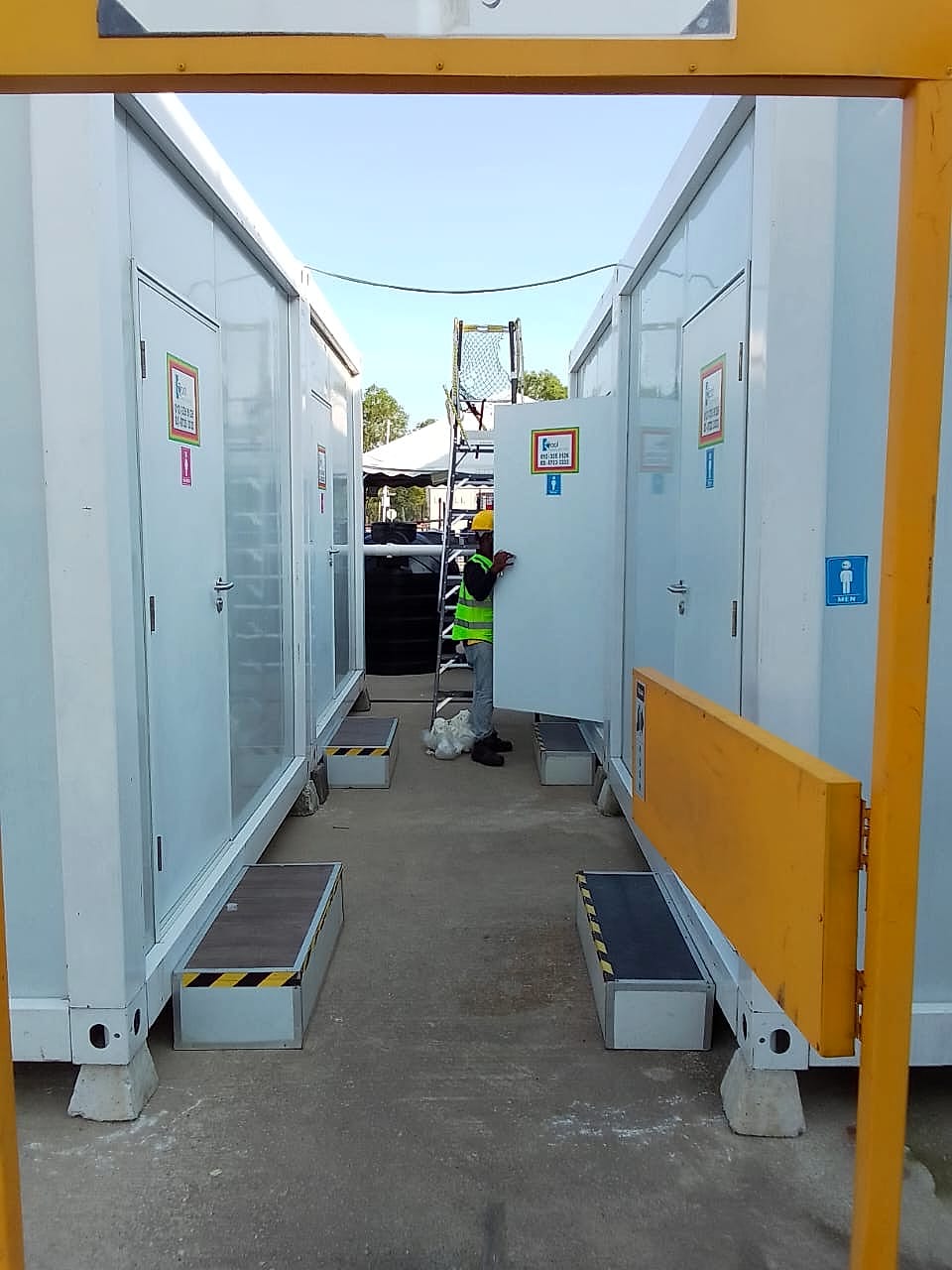 Narrow aisle between facing white container toilet cabins with a worker opening a door