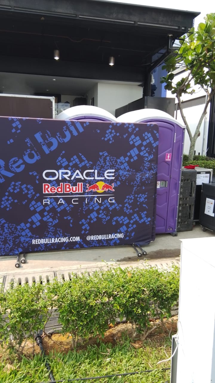 Purple EQool portable toilets beside an Oracle Red Bull Racing branded barrier at the team area