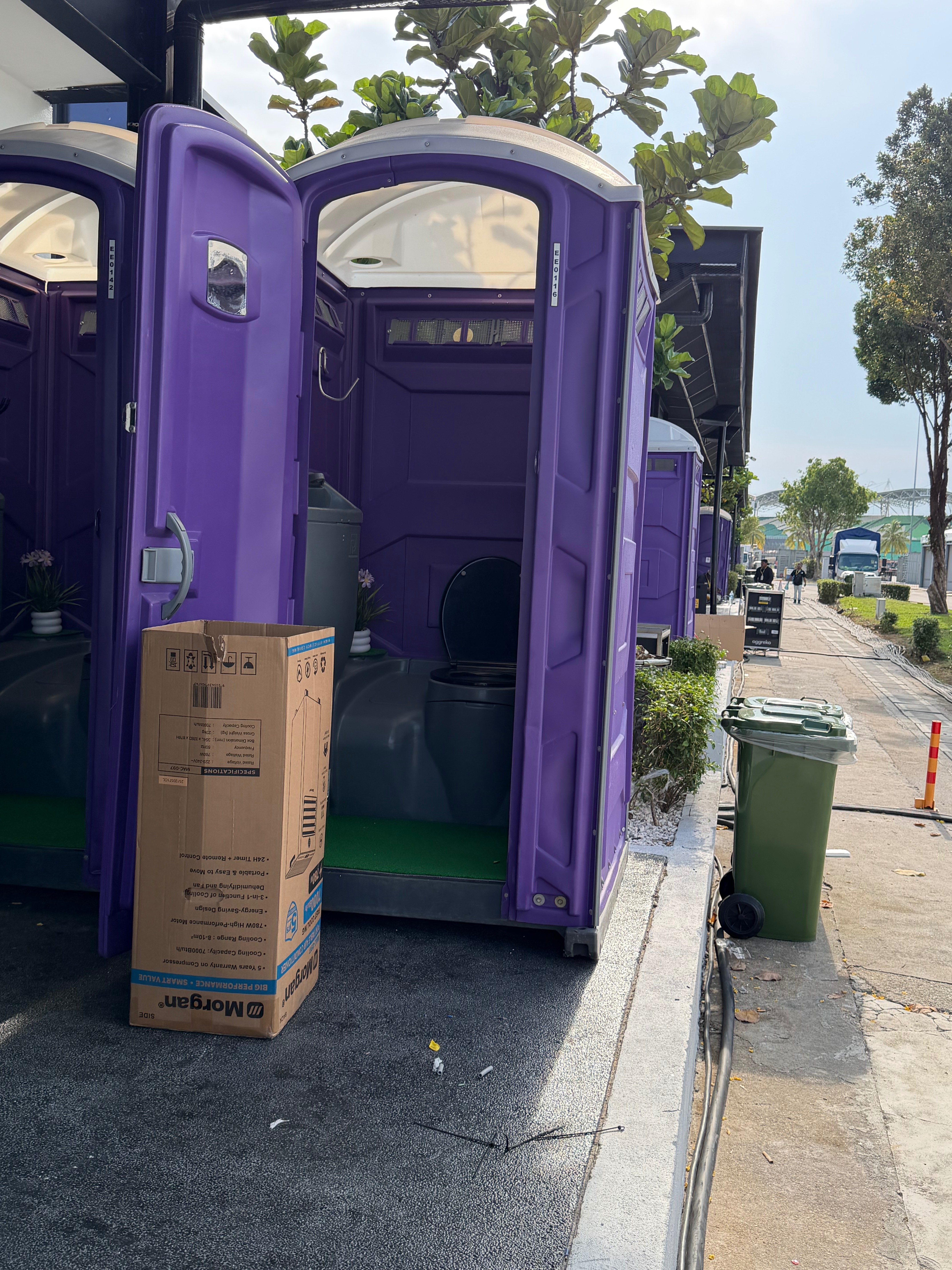 Open door of a purple EQool portable toilet showing a clean interior with green floor mat and flowers