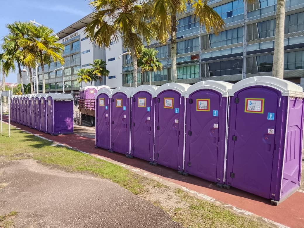 Long row of purple EQool portable toilets beside a red walking track and palm trees in Putrajaya
